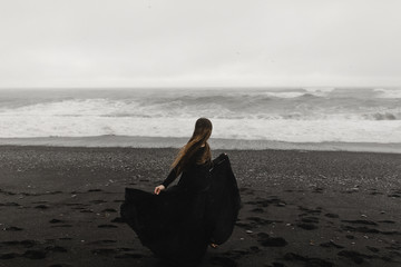 woman wearing a black dress on the black beach in iceland during a storm - 204636162