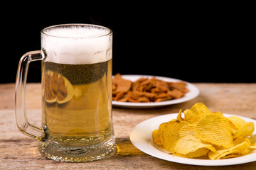 On a wooden table is a mug of beer. In the background is a plate with crispy croutons.