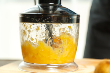 In the bowl of a blender, orange slices are crushed. next to it there are fresh oranges. horizontal photo.