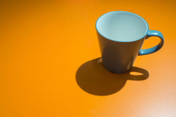 empty blue coffee cup and shadow on the yellow table with light reflection in the living room at the condominium. feeling lonely and emotional concept photo.