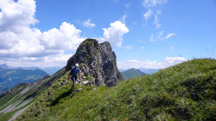 Obraz premium male climber on a grassy ridge on his way down from a climbing route with a great mountain landscape behind him