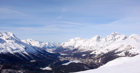 view of a winter landscape of the frozen lakes of the Engadin Valley and St. Moritz with the surrounding high alpine mountain peaks