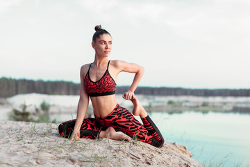 An attractive young woman doing a yoga pose for balance and stretching near the lake high in the mountains