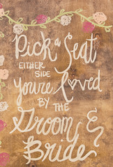 Obraz premium Pick a seat either side you're loved by the groom and bride sign 