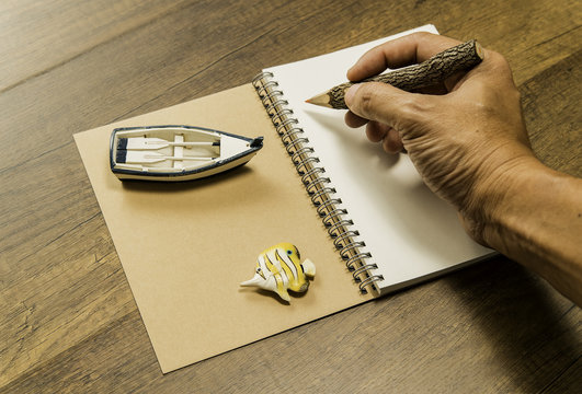Human hand holding color pencil on notebook with boat and fish