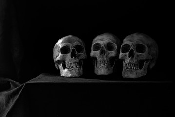 Old Three skulls put on the table which has black cloth cover in dim light room black and color for background