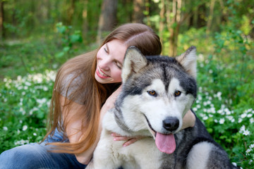 redhead young woman plays with her dog malamute on a walk in the forest