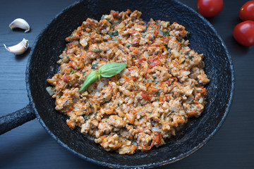 Fried ground meat with vegetables in an old frying pan on a dark background, garlic and tomatoes