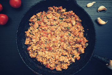Fried ground meat with vegetables in an old frying pan on a dark background, garlic and tomatoes