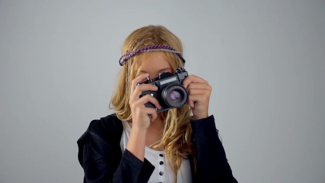 Cute blonde young girl holding an camera isolated on gray background. A teenager is smiling and taking pictures