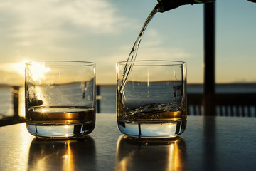 Pouring two glasses of whiskey at sunset low angle close up view.
