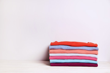 Stack of colorful perfectly folded t-shirts on white wooden texture table background. Pile of different pastel color cotton shirts and sweaters. Background, close up, front view, copy space for text.