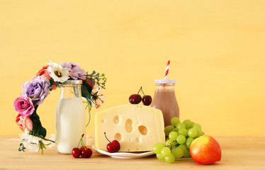 image of fruits and cheese in decorative basket with flowers over wooden table. Symbols of jewish holiday - Shavuot.