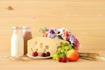 image of fruits and cheese in decorative basket with flowers over wooden table. Symbols of jewish holiday - Shavuot.