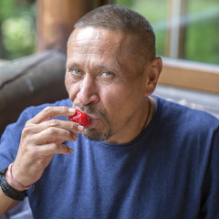 Happy middle-aged man eating a ripe red strawberry, close-up portrait