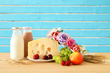 image of fruits and cheese in decorative basket with flowers over wooden table. Symbols of jewish holiday - Shavuot.