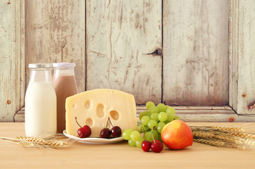 image of fruits and cheese in decorative basket with flowers over wooden table. Symbols of jewish holiday - Shavuot.