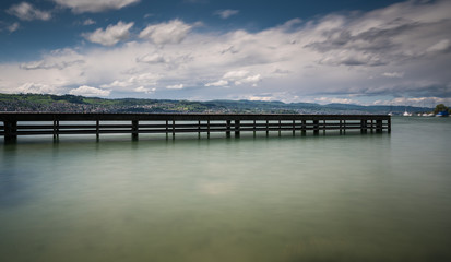 wooden pier on lake Zurich with rolling hills mountain landscape and sailboats in the background