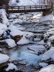 Mountain Creek Streaming Through Rocks covered with Snow and Wooden Bridge