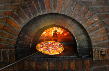 Pizza near the stone stove with fire. Background of a traditional pizzeria restaurant with a fire place.