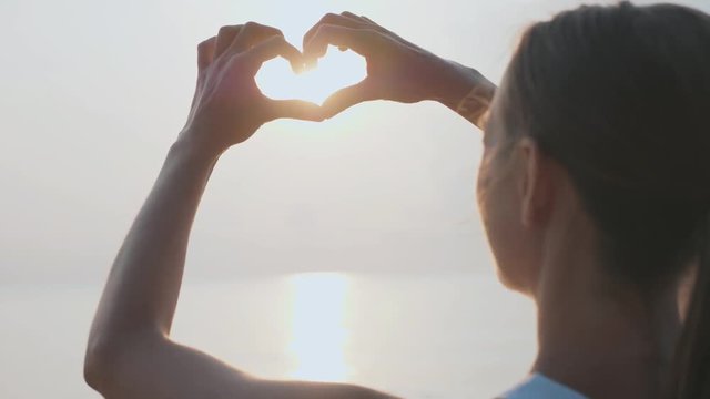 Female hands making heart shape gesture holding sun flare