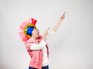 Mature woman with colorful mohawk and a smile pointing at an imaginary inscription on a gray background