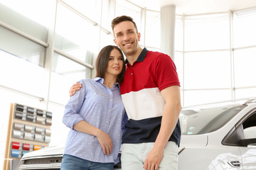 Young couple near auto in salon. Buying new car