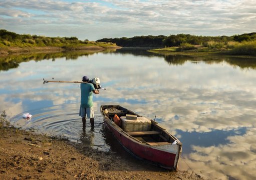 Man and small boat by the Uruguay river with clouds reflecting on water - Uruguaiana, Brazil