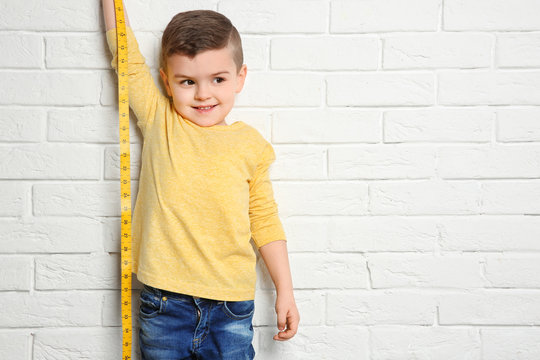 Little boy measuring his height on brick wall background