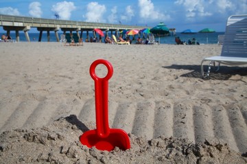 Small Red Shovel Scoop Frame Right in Sand Enclave at Deerfield Beach, Florida with Umbrellas and...