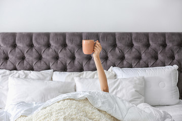 Woman with cup of coffee on bed at home