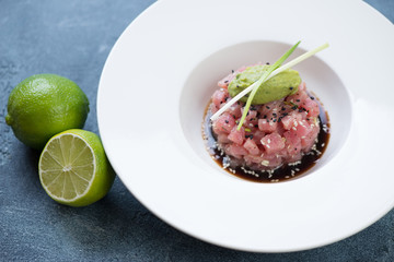 White plate with tuna tartar in soy sauce topped with guacamole quenelle and green onion, studio shot
