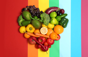 Rainbow heart made of fruits and vegetables on color background