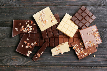 Different chocolate bars with nuts on wooden background, top view