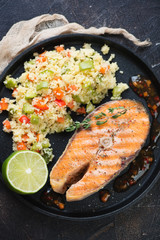 Closeup of grilled salmon steak and cuscus with vegetables, vertical shot, high angle view