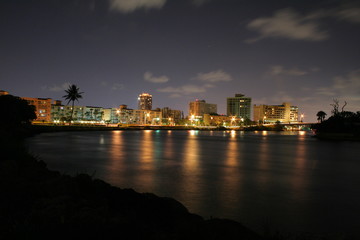 Fototapeta na wymiar Looking Westwardly at the Boca Raton City Skyline from the Intracoastal Waterway at Camino Real and SR A1A at Night in a Long Time Exposure Creating Streaks of Car Headlights and Smooth Water