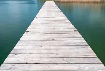 wooden pier jutting out into a turquoise and blue lake with golden reeds in the background