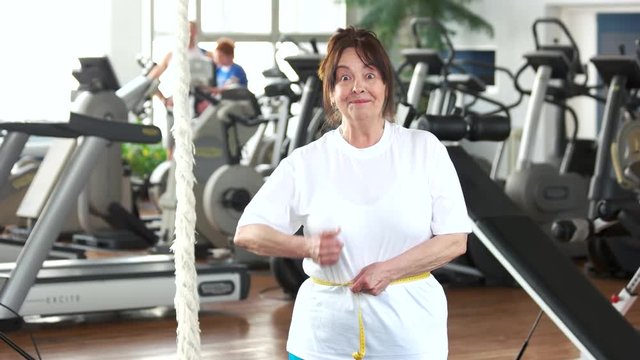 Senior woman measuring her waist at gym. Elderly woman expressing success after measuring herself with tape at fitness club. Weight loss after sport training.