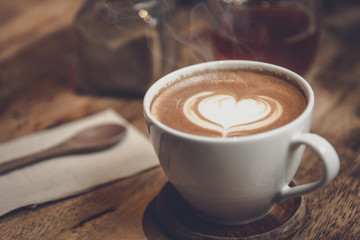 White cup of coffee with heart shape and aromatic smell on the table brown wood.