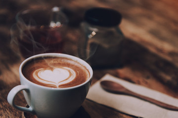 White cup of coffee with heart shape and aromatic smell on the table brown wood.