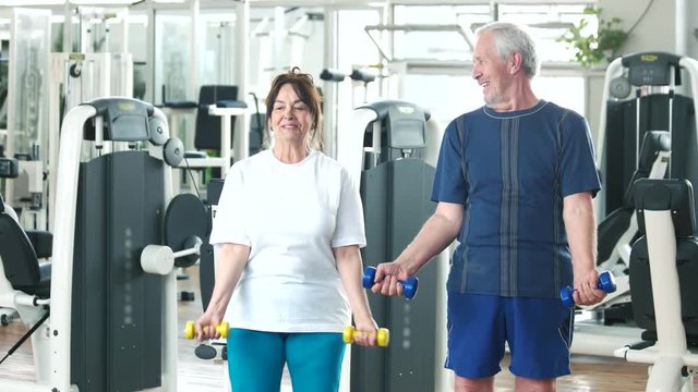 Elderly couple working out at gym. Happy senior man and woman lifting dumbbells at gym. Beautiful elderly people at fitness club.