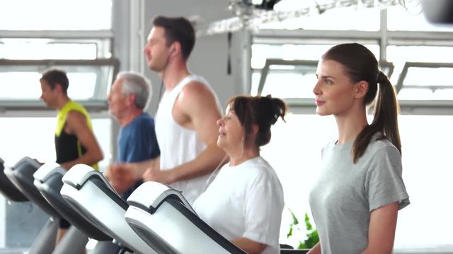 Group of people training on treadmill. Young woman exercising at gym. Sport for all ages.