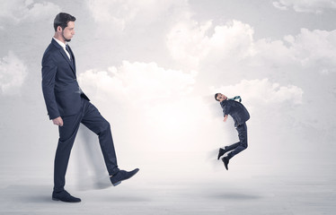 Big businessmen kicking himself as a small employee with cloudy background
