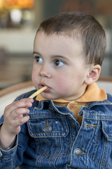 Cute little baby boy sitting at cafe eating tasty french fries. European