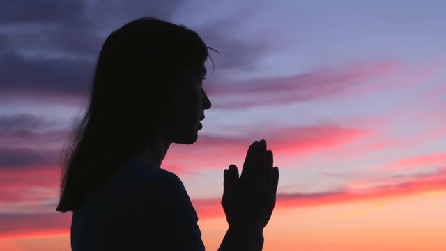 Praying girl silhouette colorful sunset. Woman with gratitude pray looking up and raising open hands to sky