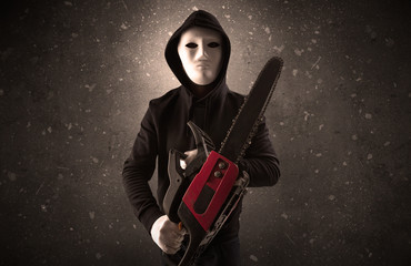 Masked armed villain in empty dark room with gun ax chainsaw mallet wrench
