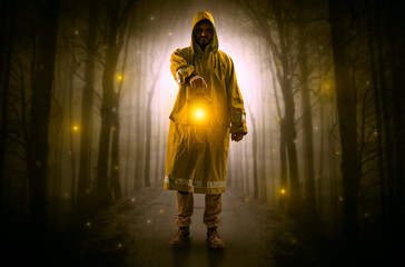 Man in raincoat coming from dark forest with glowing lantern in his hand concept
