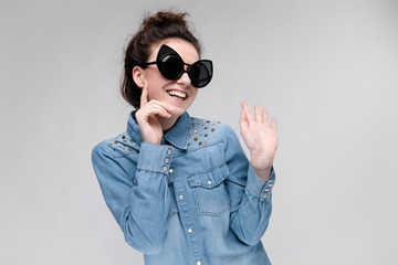 Young brunette girl in black glasses. Cat glasses. The hair is gathered in a bun. The girl put a finger to her cheek. The girl is laughing.