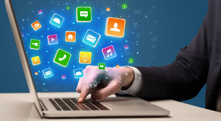 Businessman hand typing on laptop with flying application icons around
