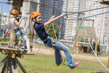 cute baby girl in climbing gear on a rope park background. Little beautiful girl climbs on rope harness in summer city park